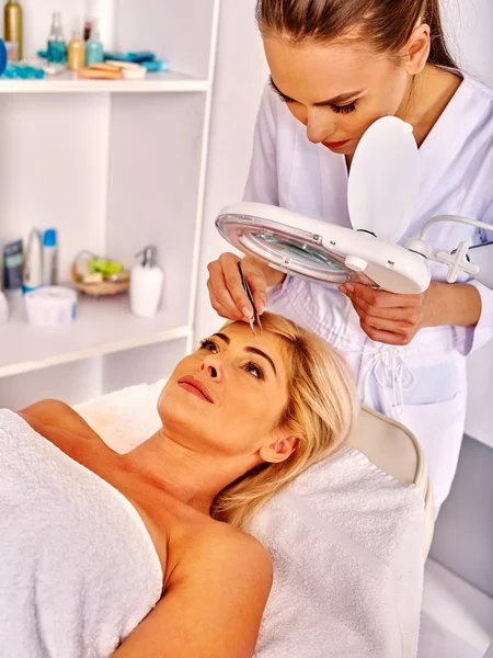 Woman middle-aged in spa salon. Tweezing eyebrow by beautician. — Stock Photo, Image