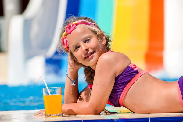Child on water slide at aquapark drinking cold squeezed orange juice. — Stock Photo, Image