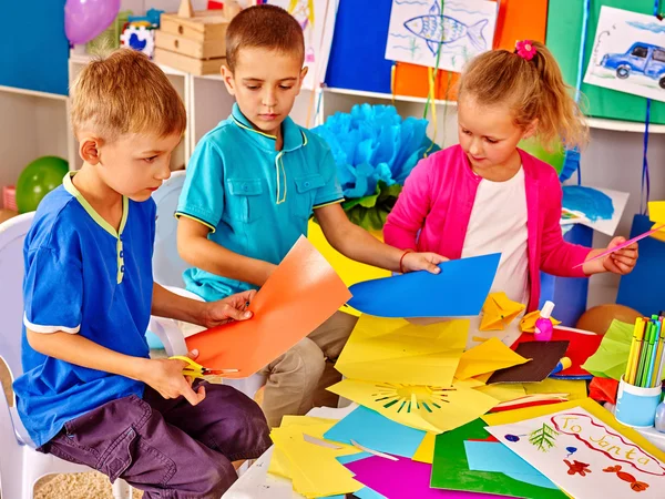 Kinder halten buntes Papier auf Tisch im Kindergarten . — Stockfoto