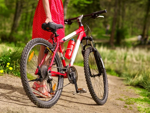 Girl wearing red polka dots dress rides bicycle into park. — Stock Photo, Image