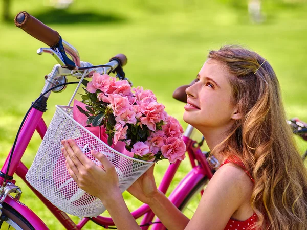 Menina vestindo passeios de sundress bicicleta com cesta de flores . — Fotografia de Stock