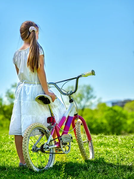 Barn tjej bär vit kjol Rider cykel i park. — Stockfoto