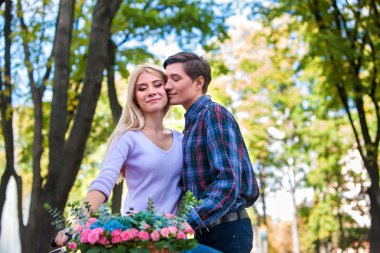 Young beautiful couple with flowers basket kissing in summer park .