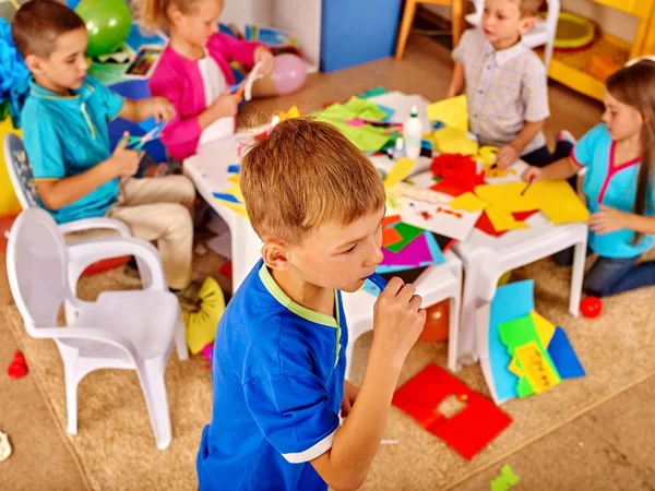 Kids holding colored paper on table in kindergarten . — Stock Photo, Image