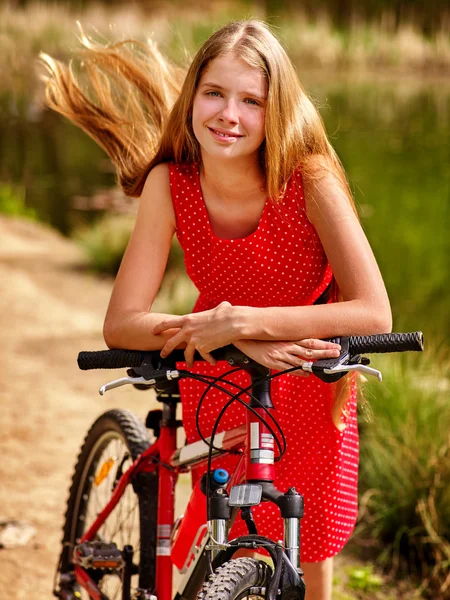 Girl wearing red polka dots dress rides bicycle into park. — Stock Photo, Image