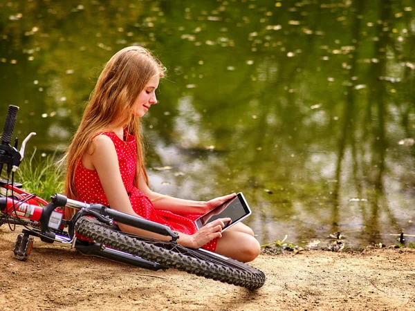 Flicka rekreation cykel och titta på TabletPC nära vatten. — Stockfoto