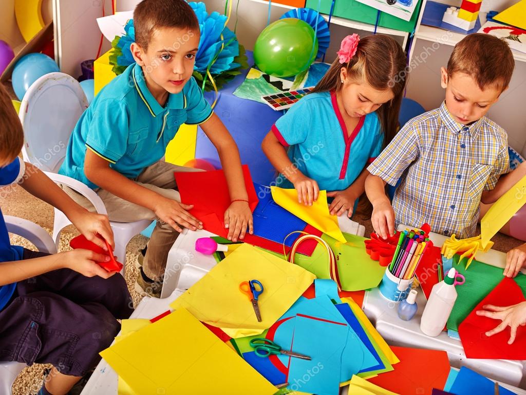 Kids working with paper on table in kindergarten . Stock Photo by