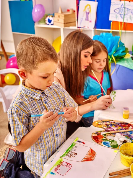 Dzieci z nauczycielem kobieta malarstwo na papierze w przedszkolu . — Zdjęcie stockowe