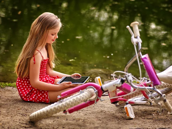 Bicyclette fille loisirs et regarder tablette PC se trouve près de l'eau . — Photo