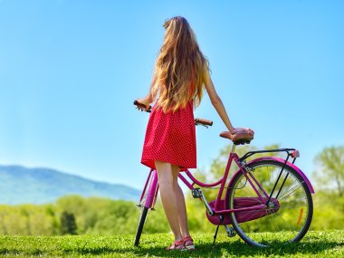 Kız giyiyor kırmızı puantiyeli elbise bisiklet ile parka doğru gidiyor.