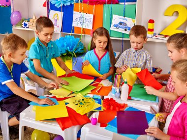 Anaokulunda masada renkli kağıt tutan çocuklar .