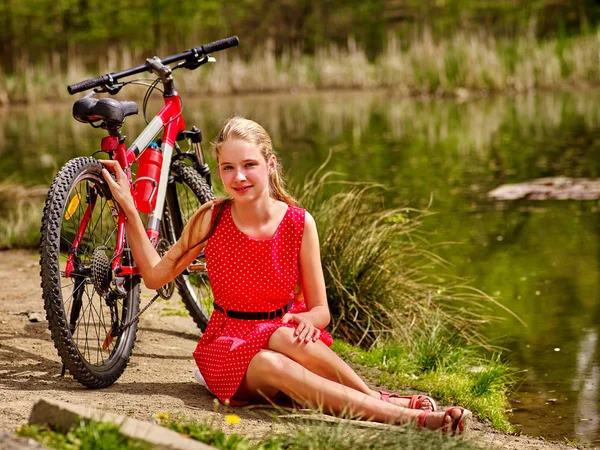 Bicicletas menina de ciclismo senta-se perto de bicicleta na costa em parque . — Fotografia de Stock