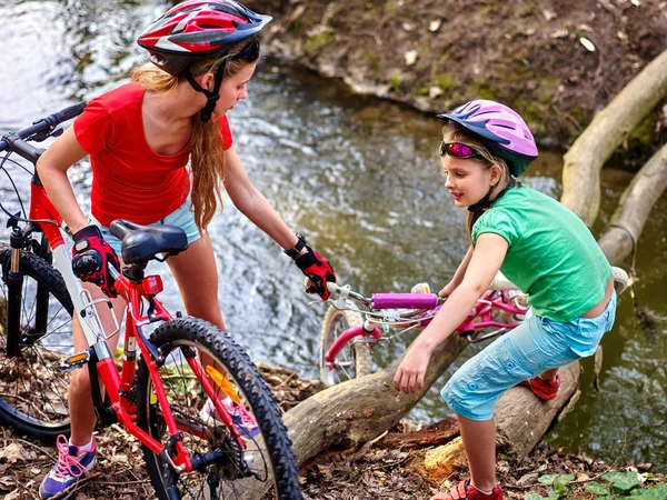 Los niños con bicicleta se ayudan mutuamente a cruzar el río en el tronco . — Foto de Stock