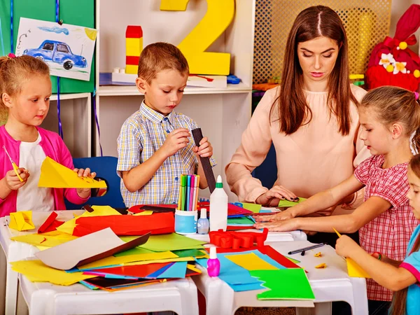 Children with teacher are making something out of colored paper. — Stock Photo, Image