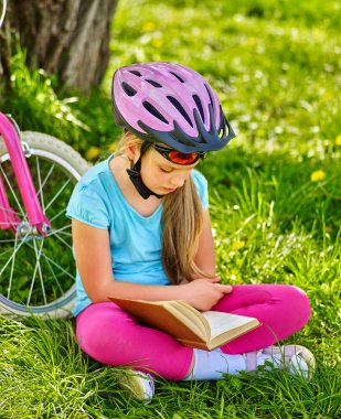 Kask giyen kız Bisiklete binme Bisiklet Bisiklet yakınındaki kitap devamını oku. .