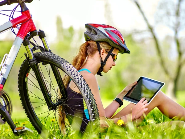 Bicicletas menina usando capacete sentado perto de bicicleta assistir pc tablet . — Fotografia de Stock