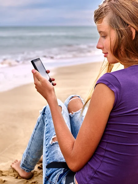 Girl with mobile phone sitting on sand near sea. — Stock Photo, Image