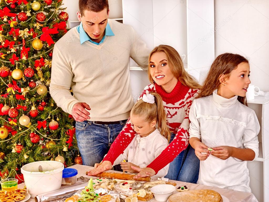 Family with children and parents rolling dough near Christmas tree.