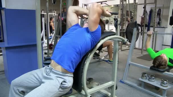 Kelompok orang di gym. Orang yang bekerja pada pelatih di gym. Di latar belakang seorang pria mengangkat barbel . — Stok Video