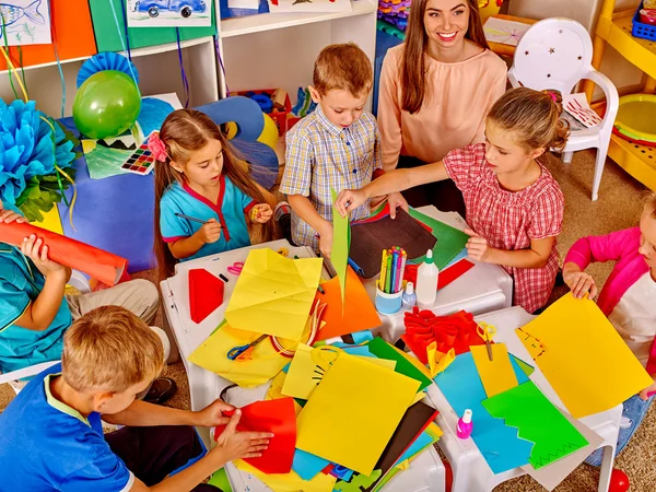 Crianças segurando papel colorido e cola na mesa no jardim de infância. Visão superior . — Fotografia de Stock