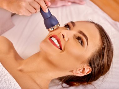 Young woman receiving electric facial massage. clipart