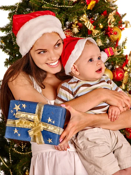 Mãe usando chapéu de Papai Noel segurando bebê sob a árvore de Natal . — Fotografia de Stock