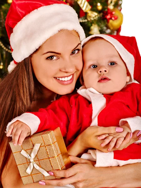 Mamá vistiendo sombrero de Santa sosteniendo bebé bajo árbol de Navidad . — Foto de Stock