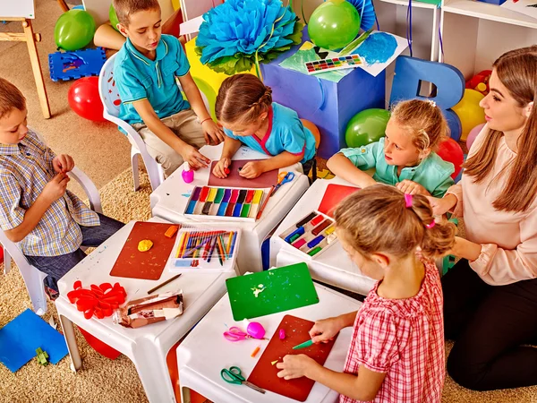 Gyerekek kezében színes papírt, és ragasztóval asztalra az óvodában . — Stock Fotó