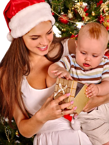 Mamá vistiendo sombrero de Santa sosteniendo niño bajo árbol de Navidad . — Foto de Stock