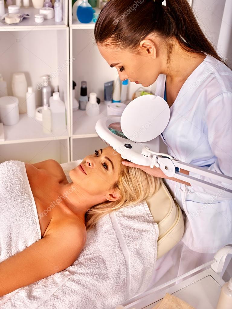 Woman middle-aged in spa salon with cosmetic lamp .