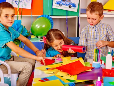 Masanın üzerine renkli kağıt tutan çocuklar