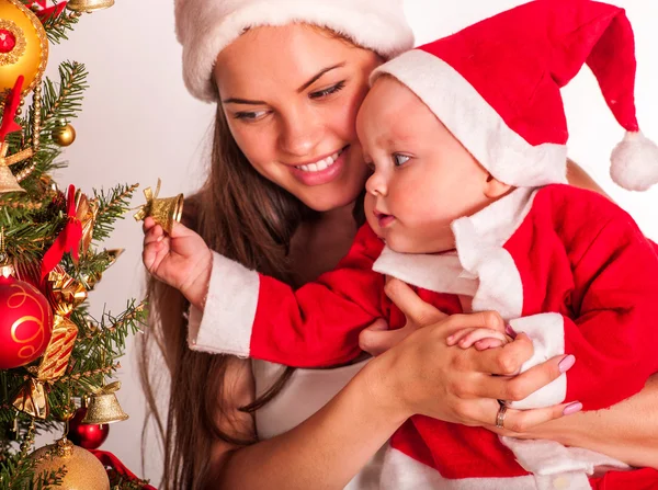 Mãe usando chapéu de Papai Noel segurando bebê sob a árvore de Natal . — Fotografia de Stock