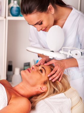 Woman middle-aged in spa salon with cosmetic lamp .