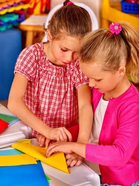 Kinder halten buntes Papier auf Tisch im Kindergarten . — Stockfoto