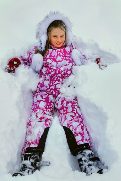 Liten flicka bär vinterkläder som ligger i snön . — Stockfoto