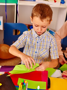 Çocuk anaokulunda masada renkli kağıt tutar .
