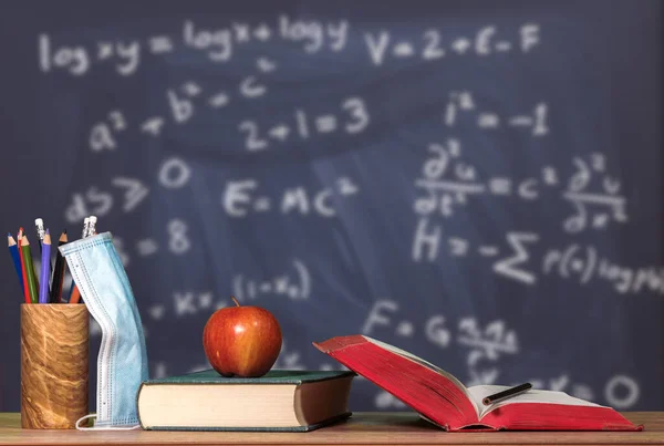 Back to virtual school background concept with stack of books, apple and face mask against math background