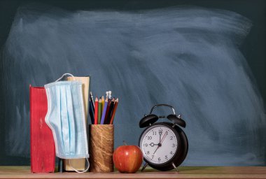 Yüz maskeli bir yığın kitap, elma ve alarmlı saat ile sanal okul arka plan kavramına dön