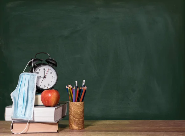 Volver a la escuela virtual concepto de fondo con pila de libros, manzana y despertador con máscara facial —  Fotos de Stock