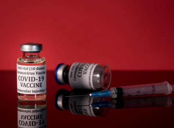Covid-19 vakcína v injekční lahvičce s injekční stříkačkou odrážející se od červeného pozadí — Stock fotografie