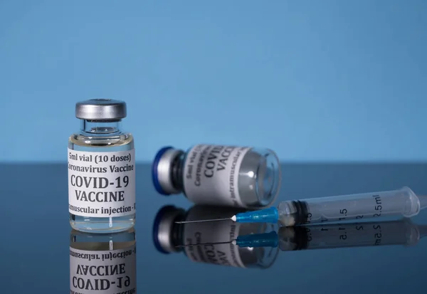 Vacuna de Covid-19 en vial con jeringa reflejada sobre fondo azul —  Fotos de Stock