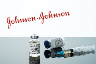 Beyaz Johnson ve Johnson 'ın arka planına yansıyan şırıngalı Covid-19 aşısı.