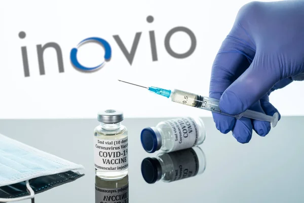 Covid-19 vaccin in flacon met spuit gereflecteerd tegen witte Inovio logo achtergrond — Stockfoto