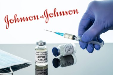 Beyaz Johnson ve Johnson logosu üzerinde yansıtılan şırıngalı Covid-19 aşısı.