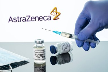 Beyaz arka planda AstraZeneca logosu üzerinde yansıtılan şırıngalı Covid-19 aşısı