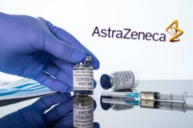 Beyaz arka planda AstraZeneca logosu üzerinde yansıtılan şırıngalı Covid-19 aşısı