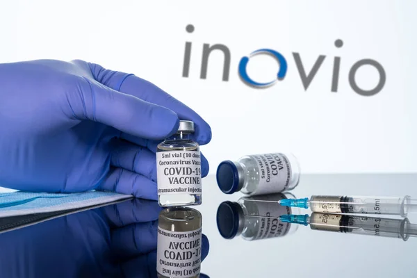 Covid-19 vaccin i injektionsflaska med spruta reflekterad mot vit Inovio logo bakgrund — Stockfoto