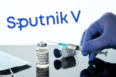 Beyaz Sputnik logosu üzerine yansıtılan şırıngalı Covid-19 aşısı.
