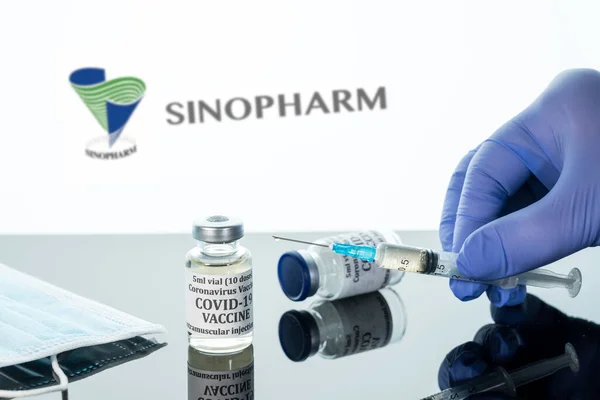 Covid-19 vaccine in vial with syringe reflected against white Sinopharm logo background — Stock Photo, Image