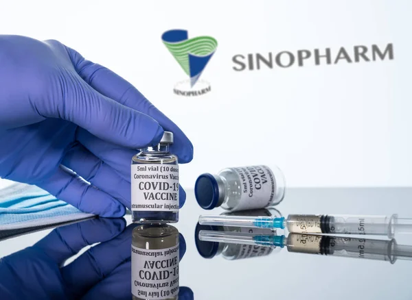 Covid-19 vakcína v injekční lahvičce s injekční stříkačkou odrážející se na pozadí bílého loga Sinopharm — Stock fotografie